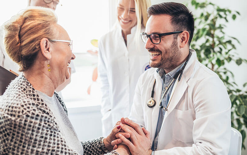 A doctor specializing in senior care services smiling with his older female patient.