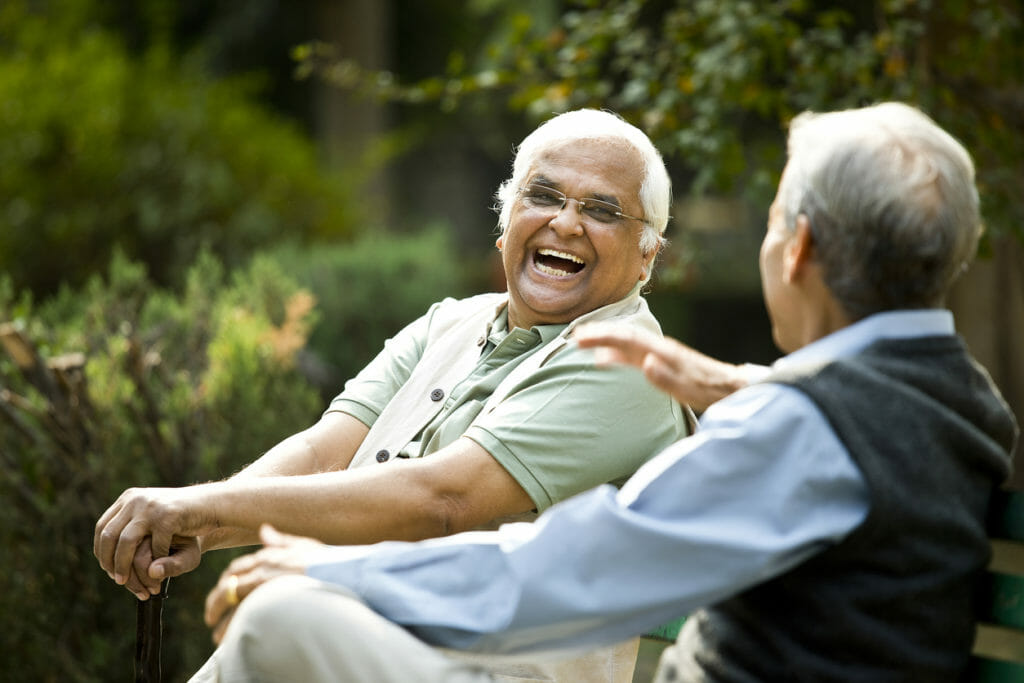 Two older gentleman sitting and laughing outside of a senior medical center.