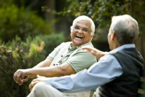 Two older gentleman sitting and laughing outside of a senior medical center.