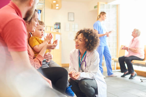 A young family sits talking to the doctor. The toddler is sat on his mother’s knee as the doctor kneels down to talk to him