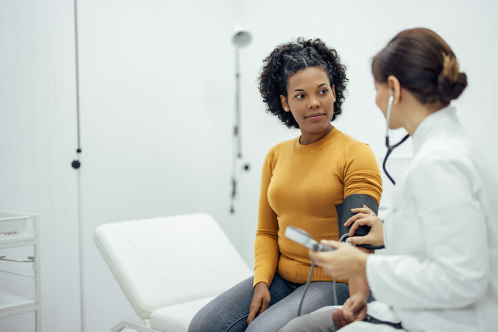 Doctor measuring blood pressure to a smiling woman at primary care clinic