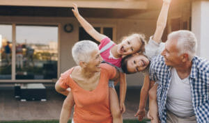 Playful grandparents having fun with their grandkids while piggybacking them in the backyard. Children are looking at camera.