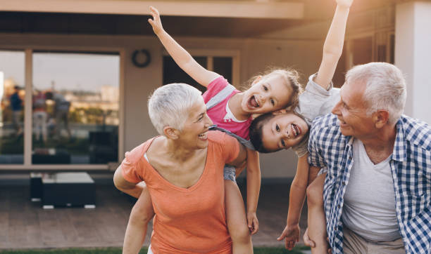 Playful grandparents having fun with their grandkids while piggybacking them in the backyard. Children are looking at camera.