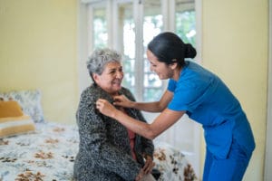 nurse helping senior woman dress shirt in bedroom