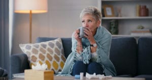 sick senior woman with a flu and medicine on her living room sofa at home