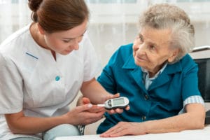 A young female doctor is performing a blood sugar test on her elderly patient to check for diabetes.