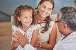 A pediatrician gives a high five to a happy girl patient and her mother during a health checkup at a primary care clinic.