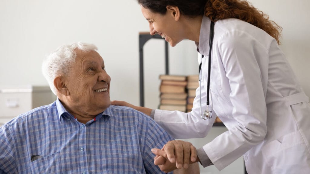 A friendly female caregiver provides support to an older male with a severe diagnosis.