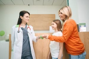 Imagine a mother shaking hands with a pediatrician for her little daughter at a primary care clinic.