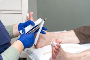 A close-up of a nurse cutting gauze to perform curettage on an elderly patient's foot.