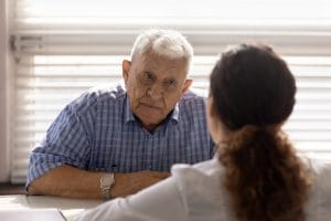 An elderly man is listening to his psychiatrist at a meeting for senior mental health care.