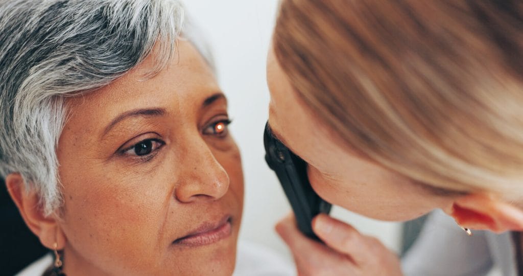 An optometrist examines an elderly woman using a retinoscope in a clinic for her eye exam, focusing on healthcare and vision.