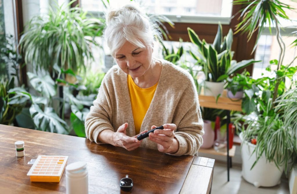Elderly woman checking her blood sugar level for diabetes while sitting at home.