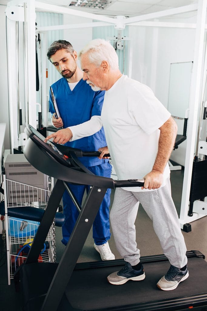 An elderly man is participating in a fall prevention program with the assistance of a physical therapist.